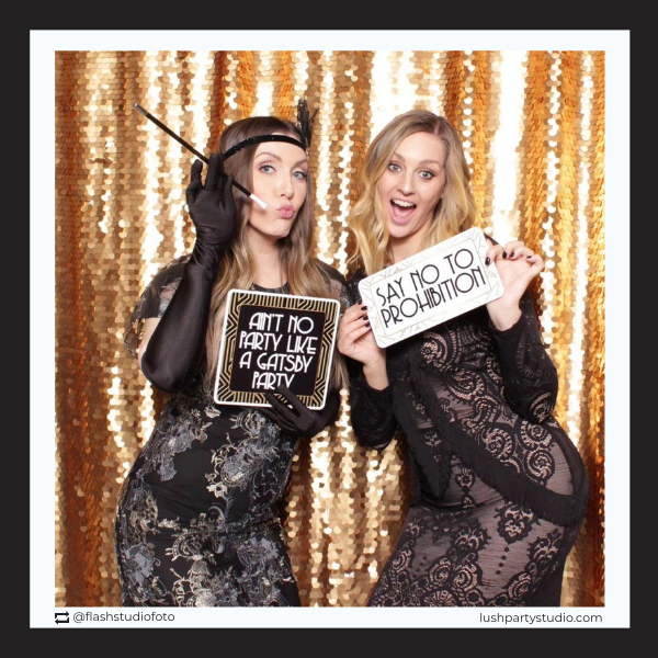 Two women in formal attire with great gatsby photo prop signsby lush party studio