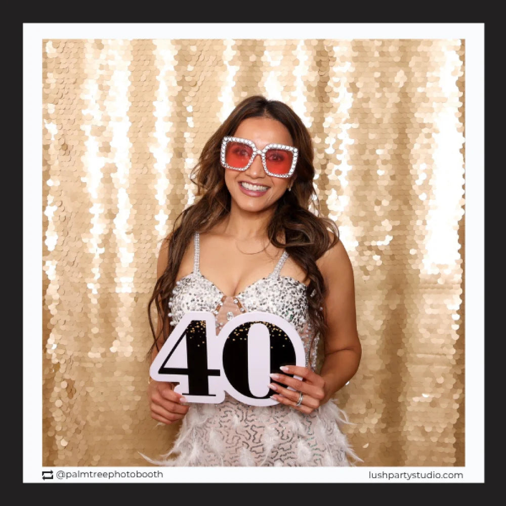 Woman in a sequin dress holding a '40' photo booth prop sign by lush party studio