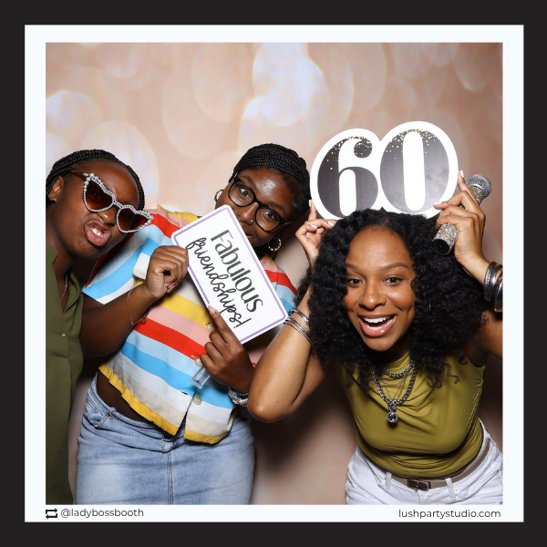 Three women posing with photo booth props including a 'Fabulous Friends Forever' sign and a '60' number