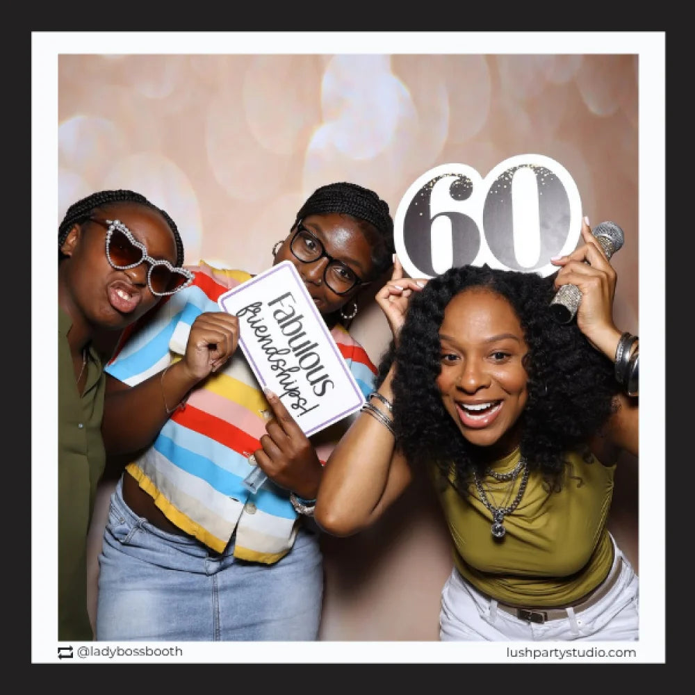 Three women posing with photo booth props including a 'Fabulous Friends Forever' sign and a '60' number