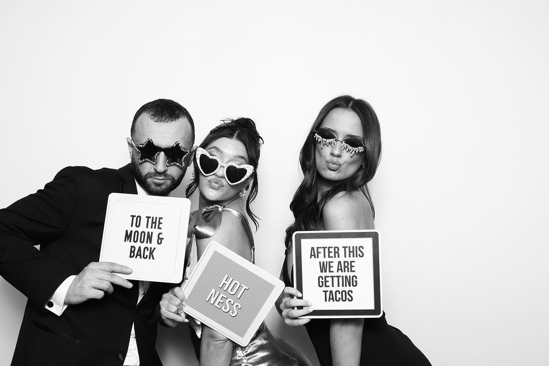 Three people holding signs with humorous text in a photo booth setting.