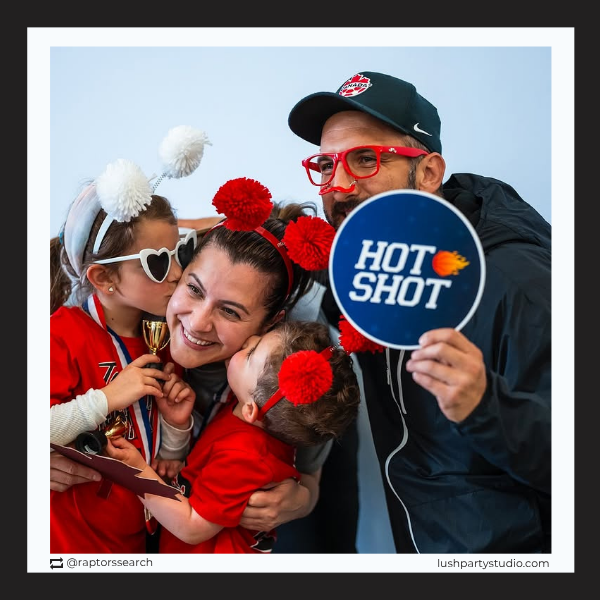 Family posing with a 'Hot Shot' photo booth prop sign and sports-themed events