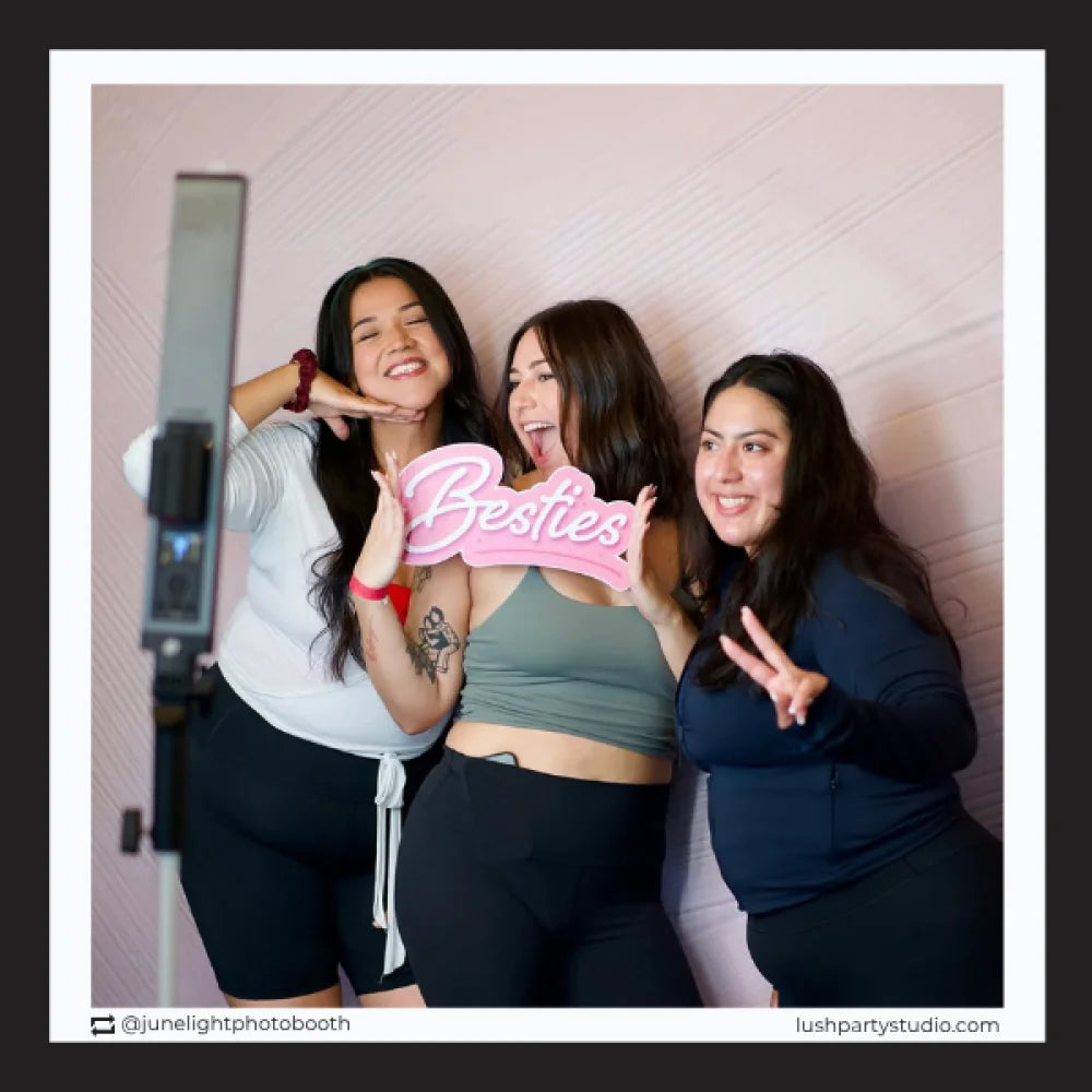 Three women posing with a 'Besties' photo booth prop sign by Lush Party Studio