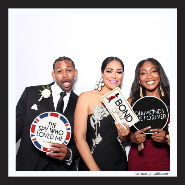 Three people in formal attire holding James Bond-themed props against a white background.