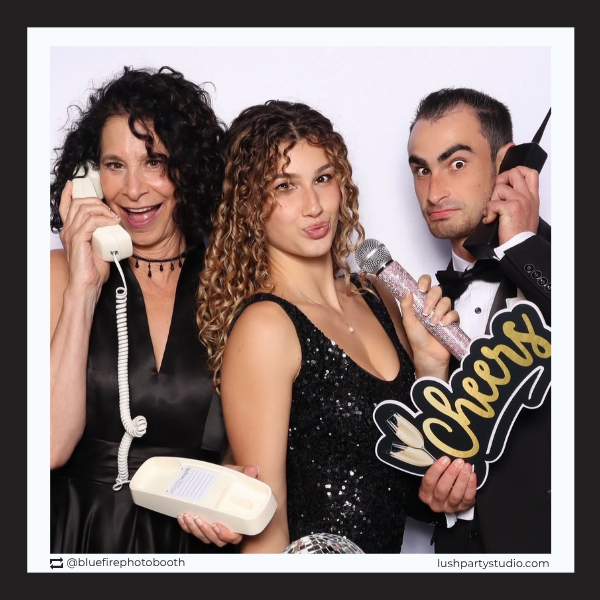Three people posing with cheers prop in a photo booth 