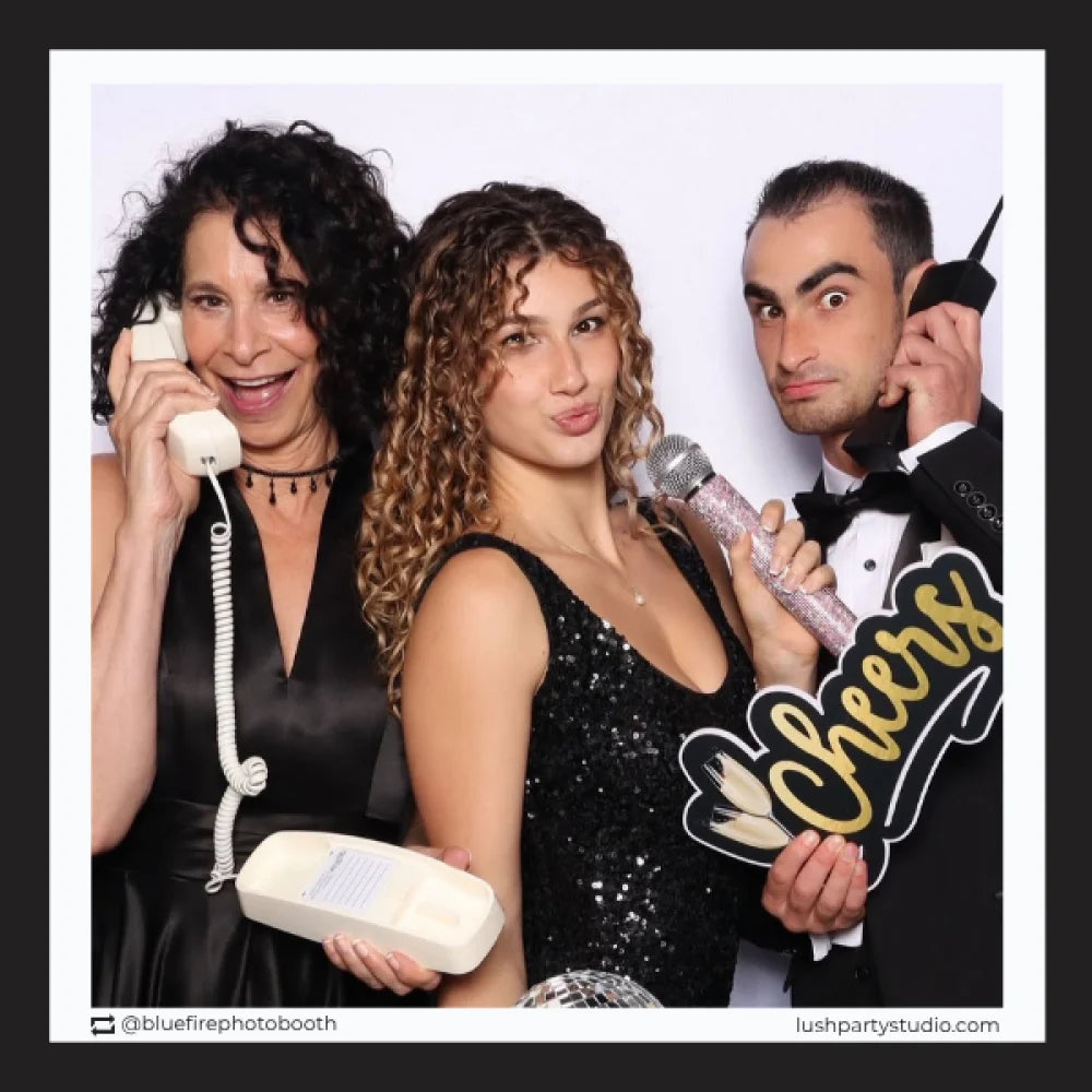 Three people posing with cheers prop in a photo booth 