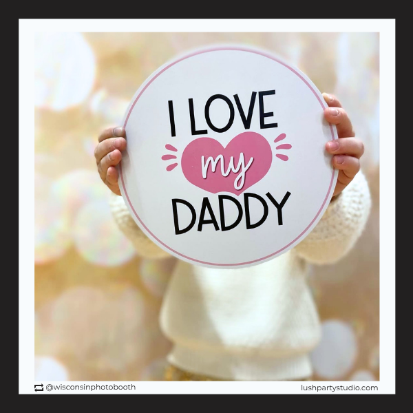 girl holding a photobooth prop sign with 'I love my daddy' text
