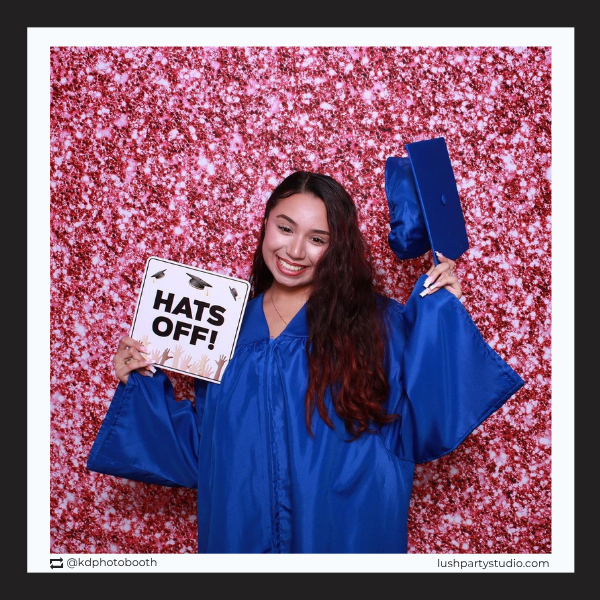 Graduate in blue gown holding a 'Hats Off!' photo booth prop sign by lush party studio