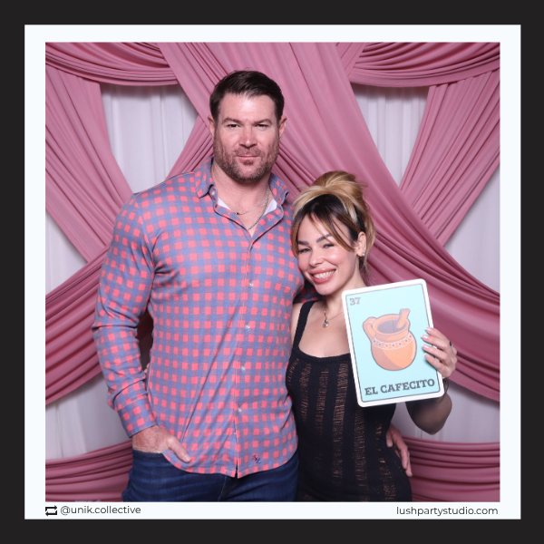 Two people posing with a loteria prop sign at photo booth