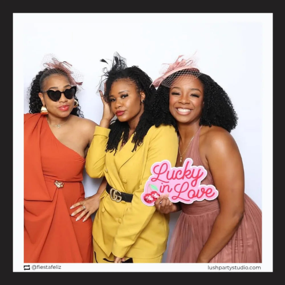 Three women posing together with a 'Lucky in Love' wedding prop sign