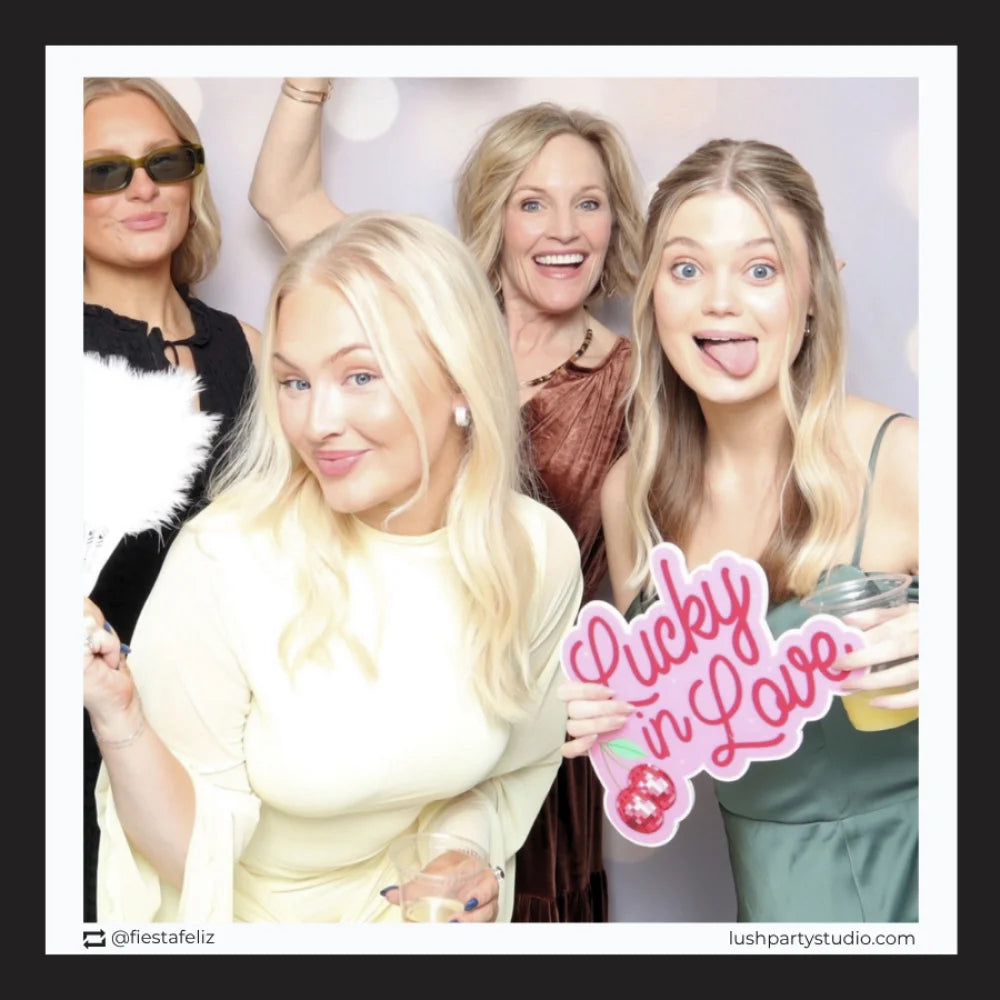 Four women posing together with a 'Lucky in Love' sign in a photo booth setting.
