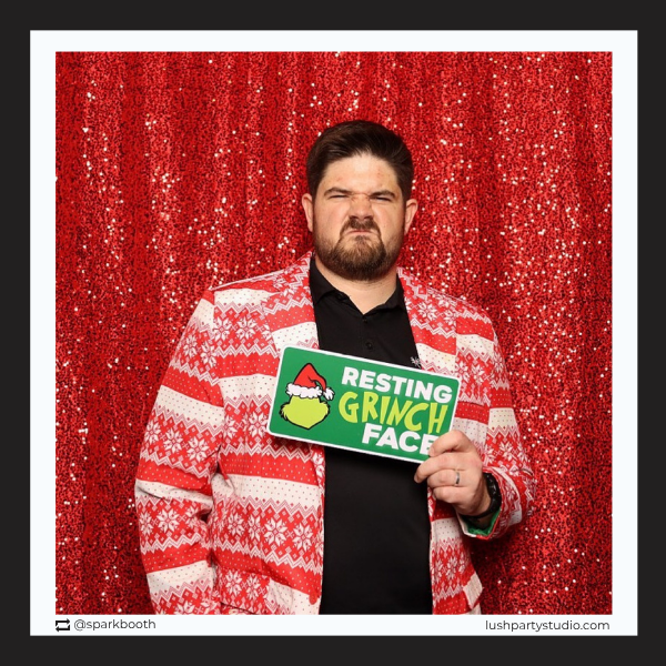 Man holding a 'Resting Grinch Face' sign at a xmas party photo booth