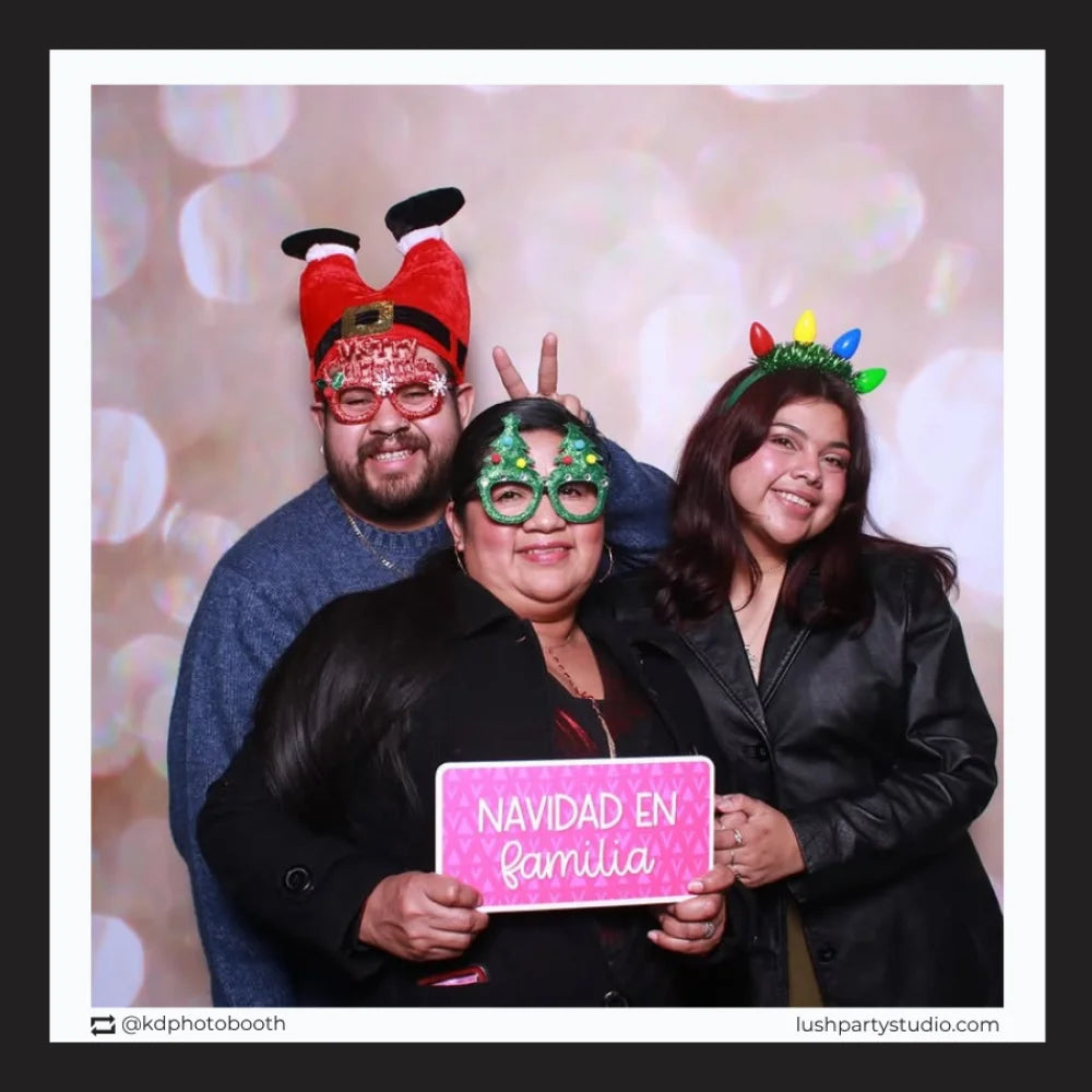 Three people posing with festive hats and glasses in a photo booth with a 'Navidad en familia' christmas prop sign.