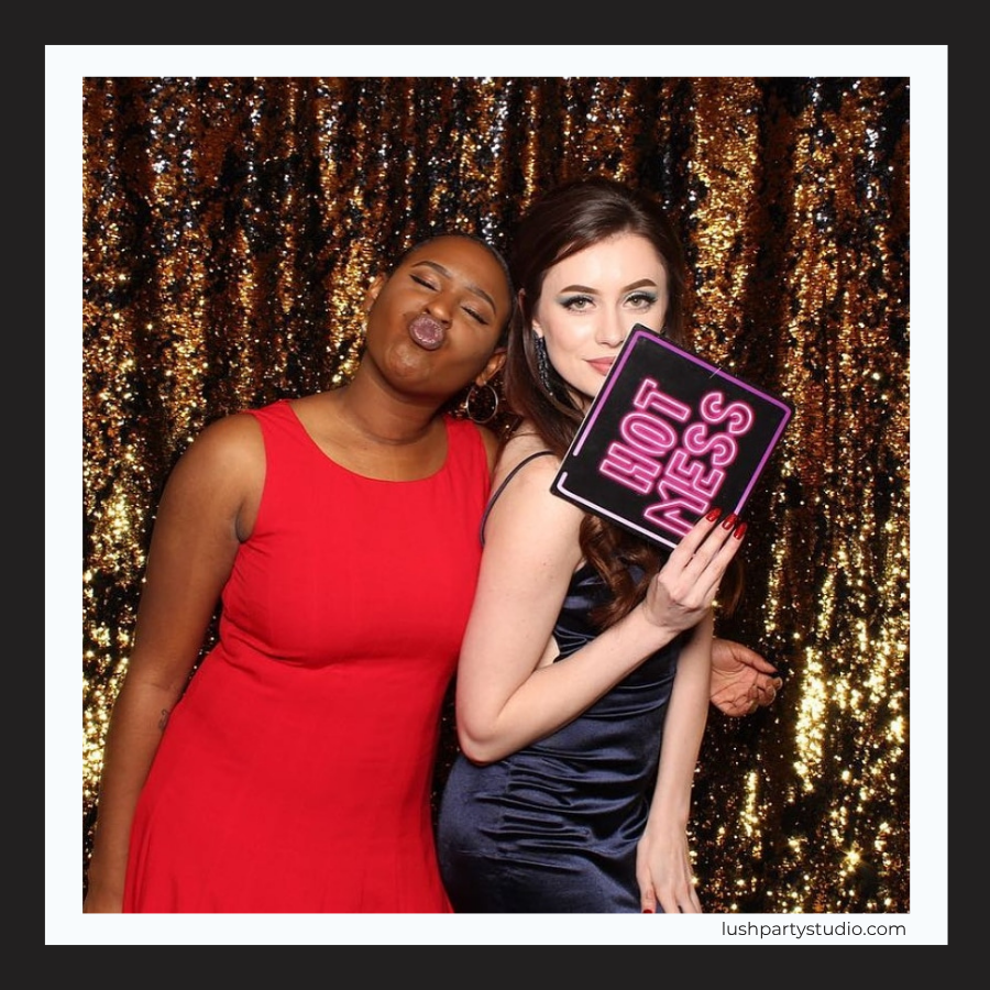 Two women posing with a neon photo booth prop sign sign by lush party studio