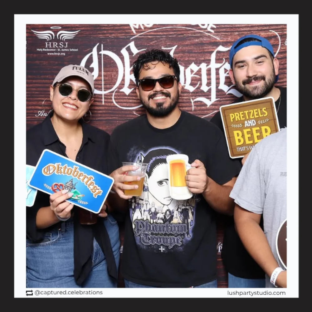 Three people posing with beer and Oktoberfest-themed photobooth prop signs by lush party studio