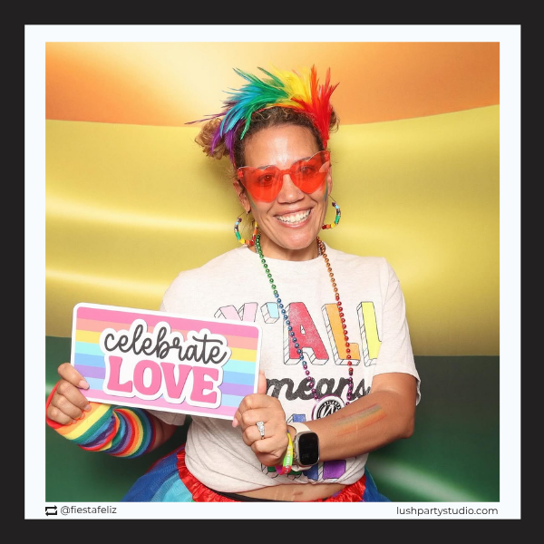 Person celebrating Pride Month with photo booth prop sign with 'celebrate LOVE' text by lush party studio