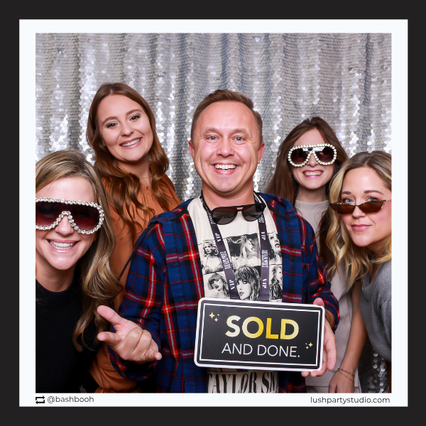 Group of people posing with a 'SOLD AND DONE' prop sign in photobooth