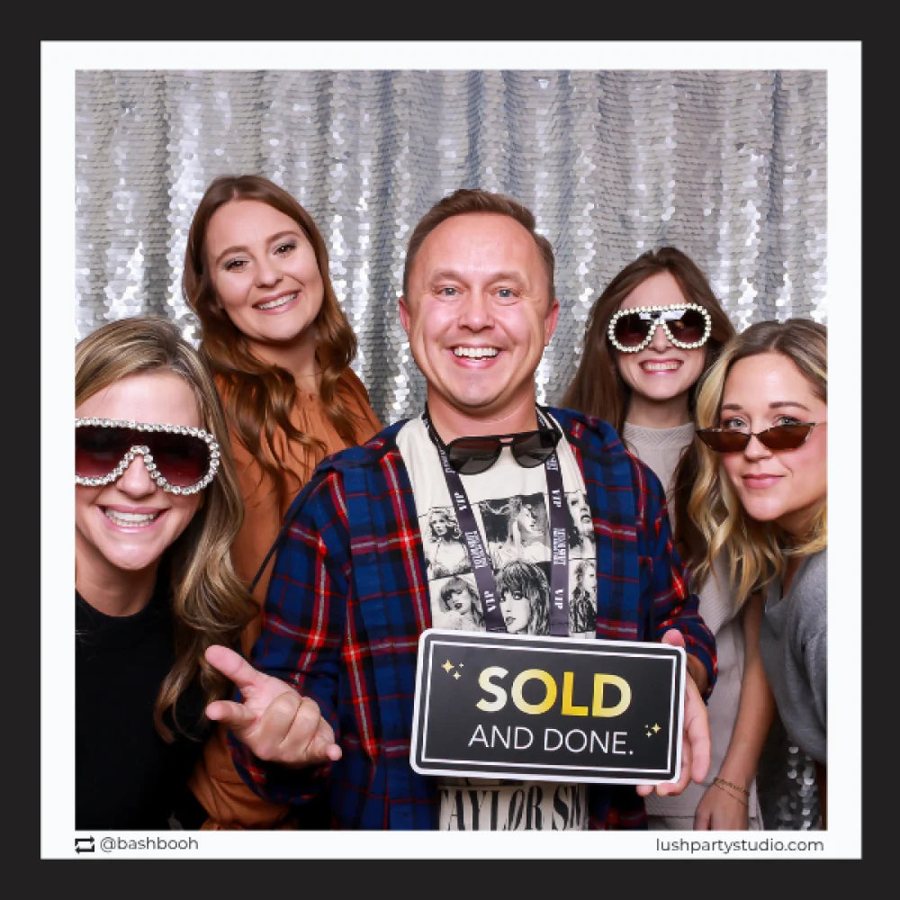 Group of people posing with a 'SOLD AND DONE' prop sign in photobooth