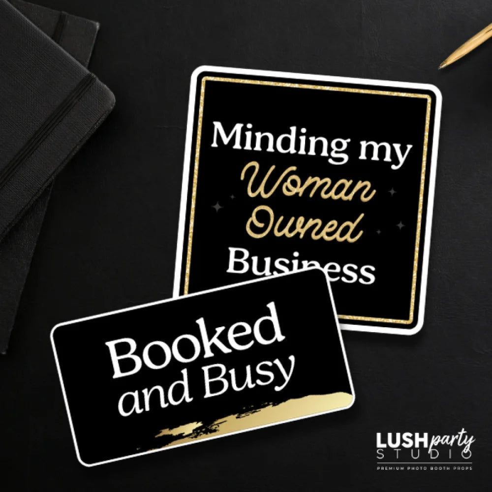 Two black and gold photo booth prop signs with 'booked and busy' text for business events