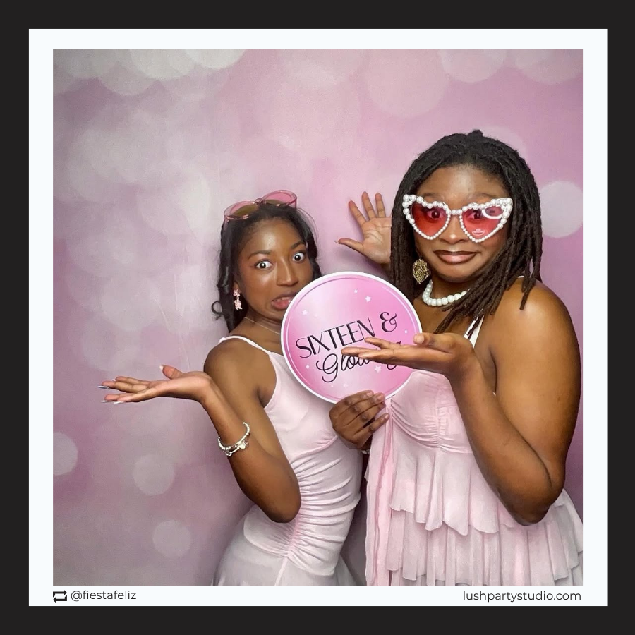 Two women posing with a 'Sixteen & Glowing' photo booth prop sign for sweet 16 party