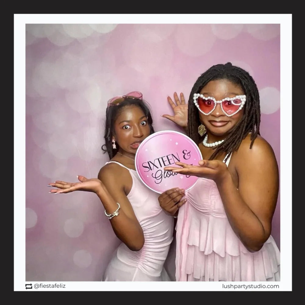 Two women posing with a 'Sixteen & Glowing' photo booth prop sign for sweet 16 party