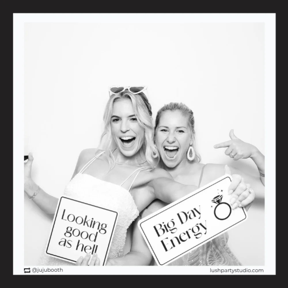 Two women posing with wedding photo booth prop signs in a photo booth, glam vogue wedding props