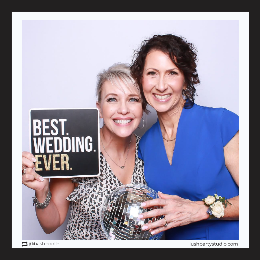 Two women holding a disco ball and a photo booth prop sign that reads 'Best Wedding Ever' by Lush Party Studio