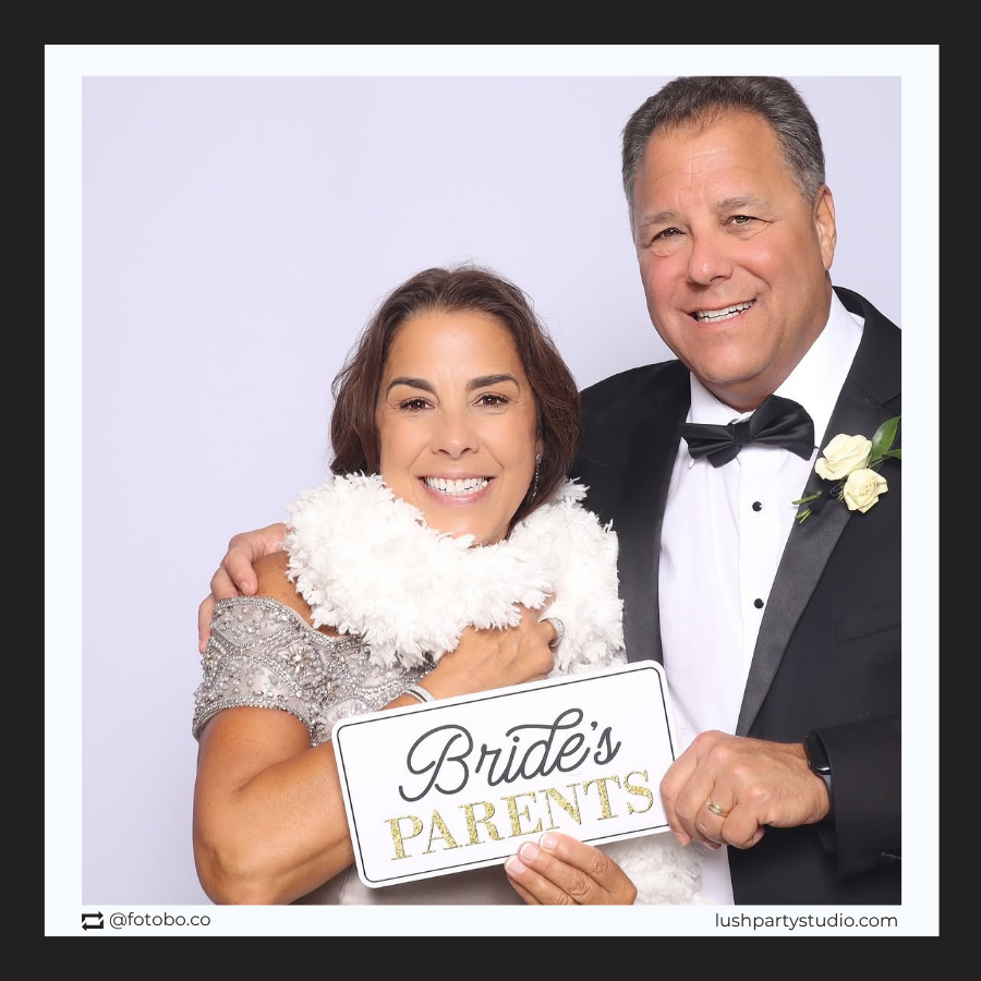 man and woman holding photobooth prop signs for bridal party with text 'Bride's parents' text.