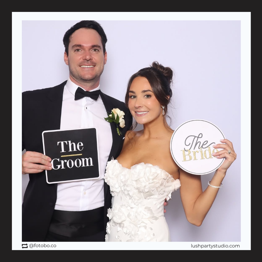 Man in tuxedo and woman in wedding dress holding signs labeled 'The Groom' and 'The Bride'photo booth props by lush party studio
